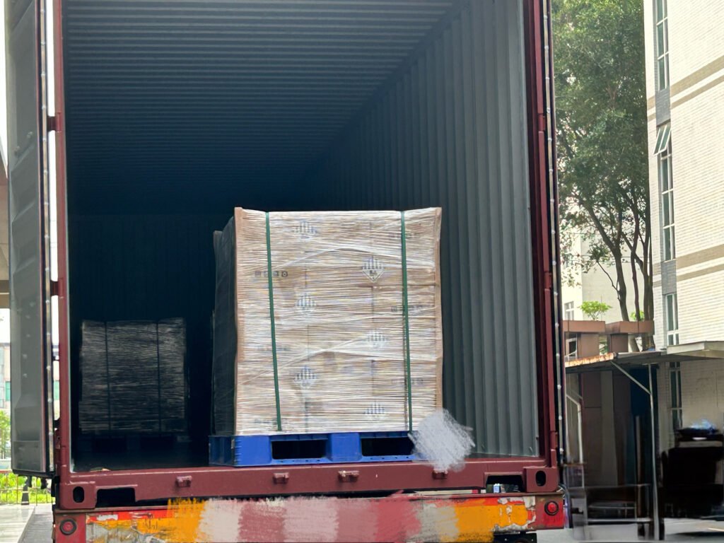 A pallet of SK On E777 battery cells positioned inside a shipping container, awaiting further arrangement by workers.