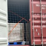 SK On E777 battery pallets secured with orange lashing straps and white safety netting inside a shipping container.