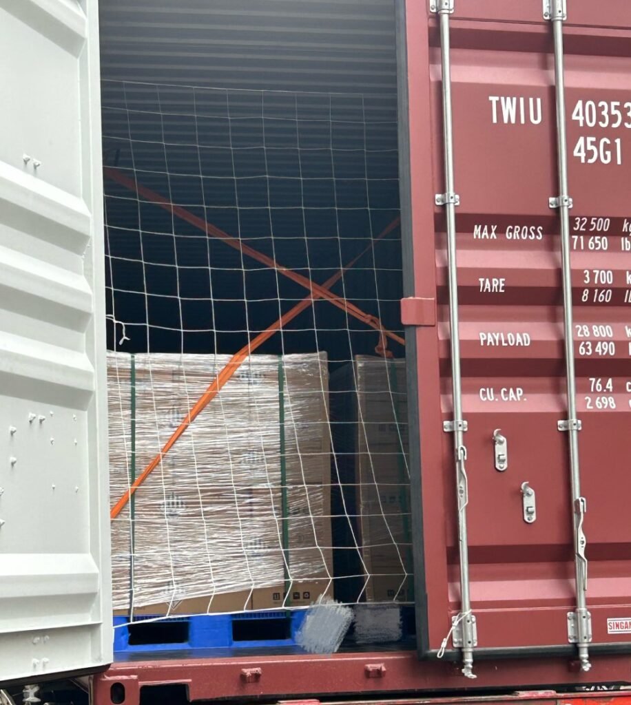 SK On E777 battery pallets secured with orange lashing straps and white safety netting inside a shipping container.