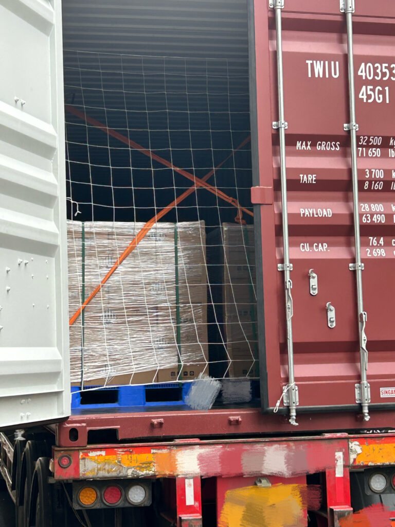 Open shipping container doors revealing SK On E777 battery pallets secured with orange lashing straps and a safety net.